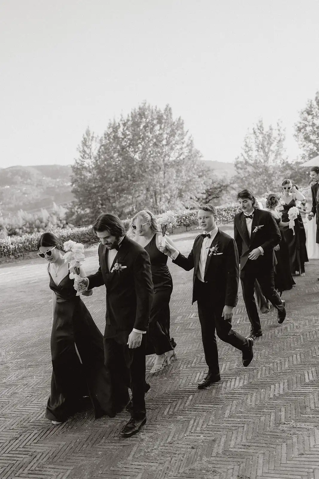 Bridal party walking with the couples side by side while they leaving the ceremony. Black and white photo, with saturated black. Portugal Minho landscapes as background.