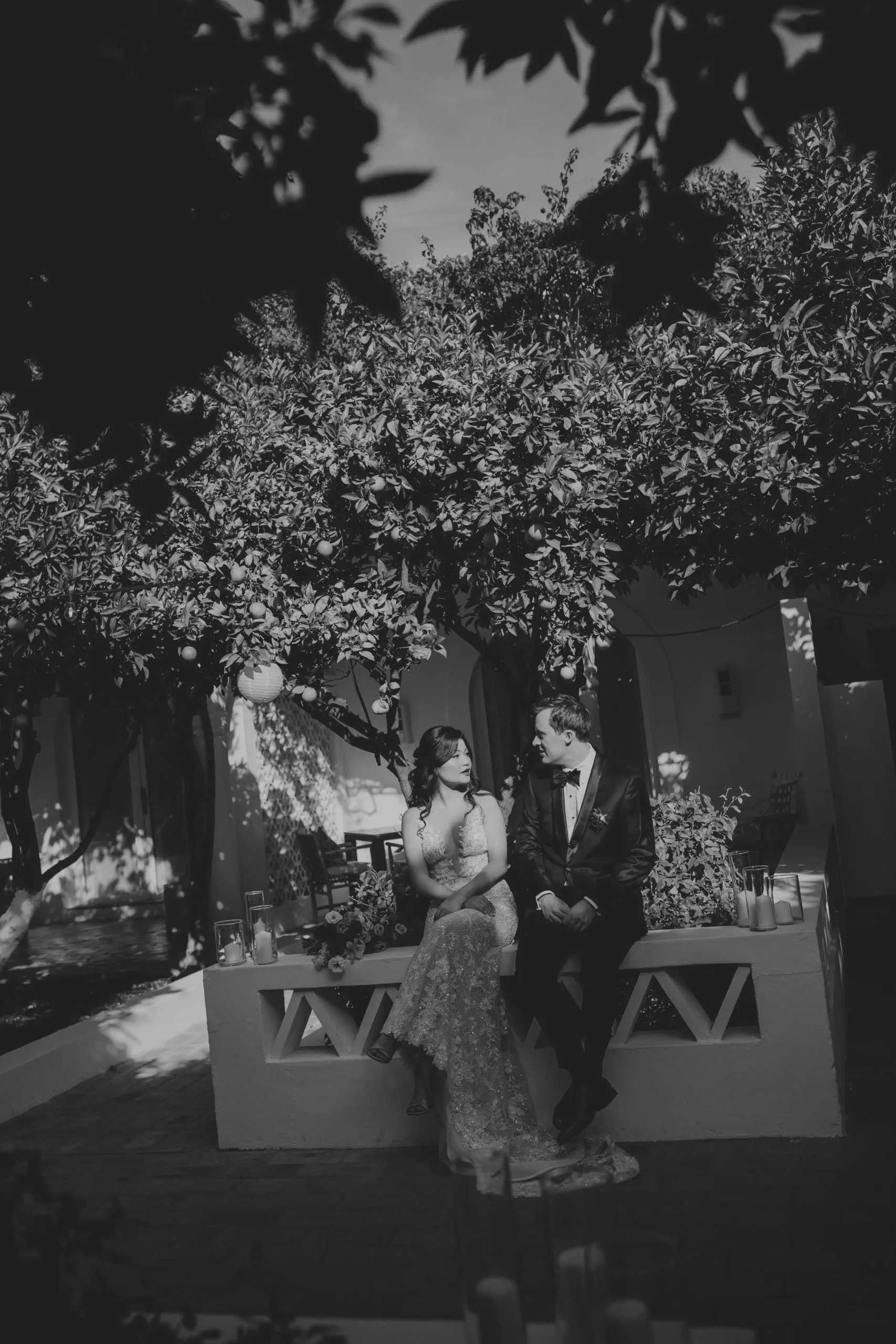 The bride and groom are sitting on a wall, looking at each other. A moment of relaxation for the couple as they wait to enter the dinner reception. Typical Algarve architecture serves as the backdrop. Black and white edition.