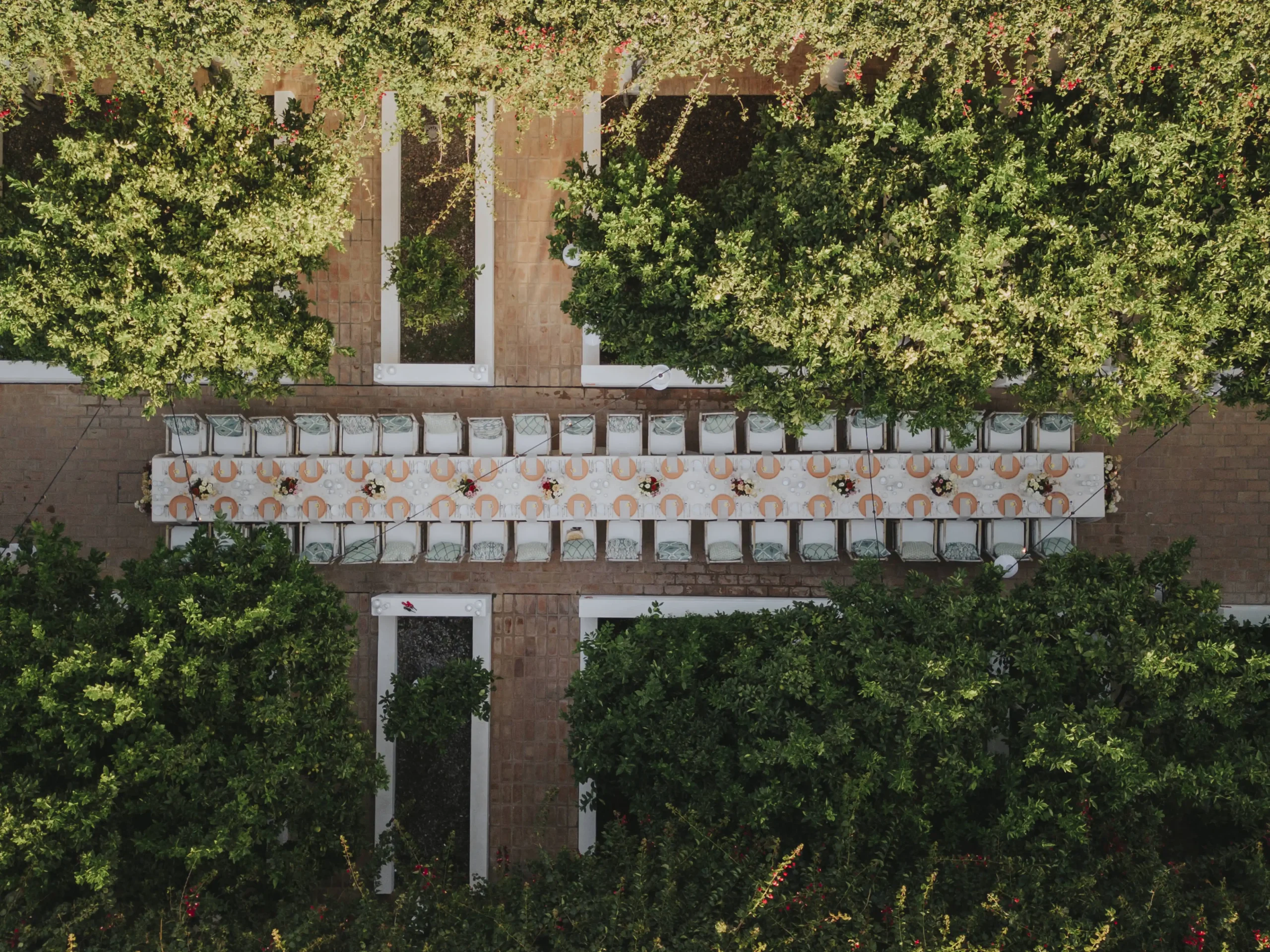 Aerial view from the wedding reception in the garden with typical Algarve architecture, surrounded by trees. Minimal colorful table decor, long tables. Portugal wedding venue.