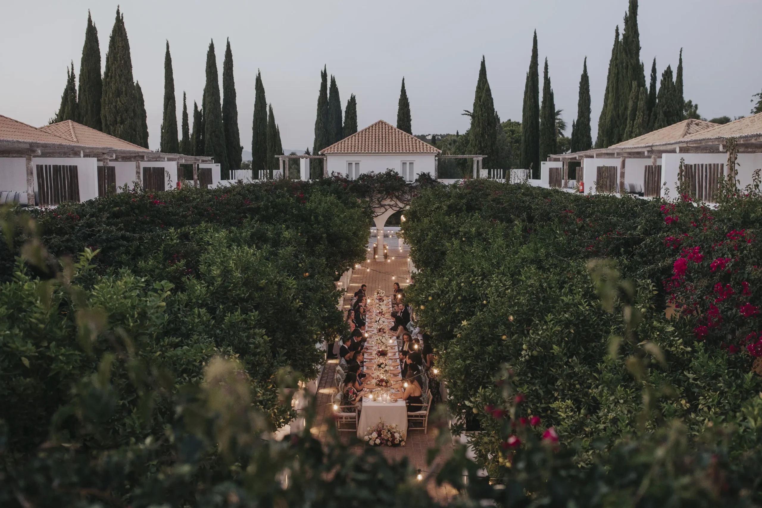 Wide angle from above showing the entire garden, between the dorms, where wedding dinner is happening. Long table dinner setup with string lights, surrounded by the trees. Intimate wedding in Portugal.