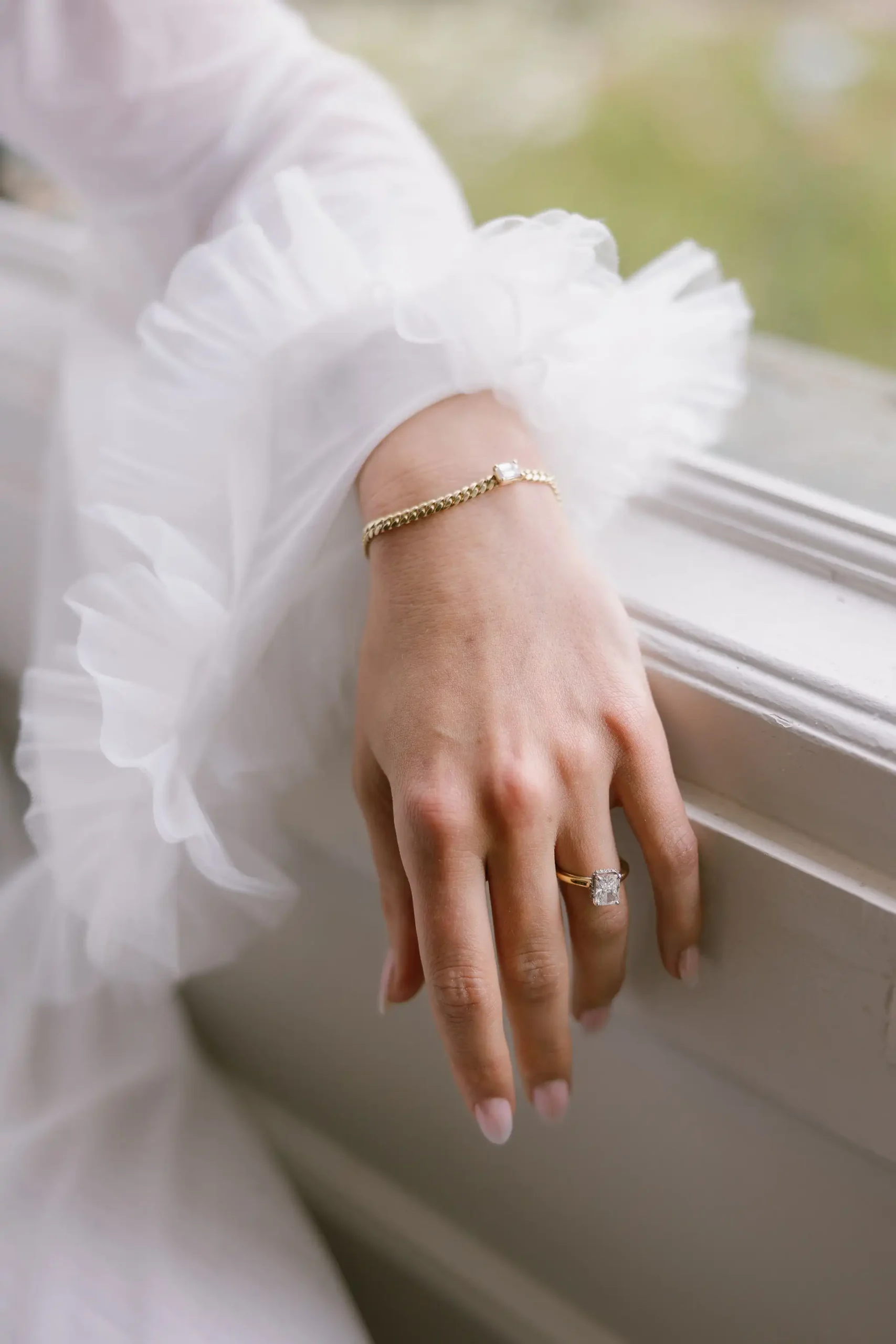 Bridal hand close-up with jewels and ruffled translucid robe sleeve.