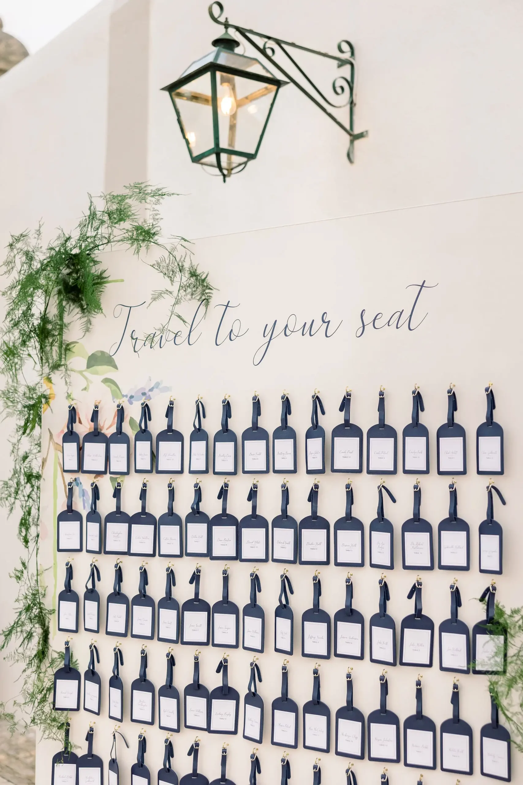 Wedding seating chart. Seating chart light pink wall with dark blue travel tags with guest names. Travel to your seat message.