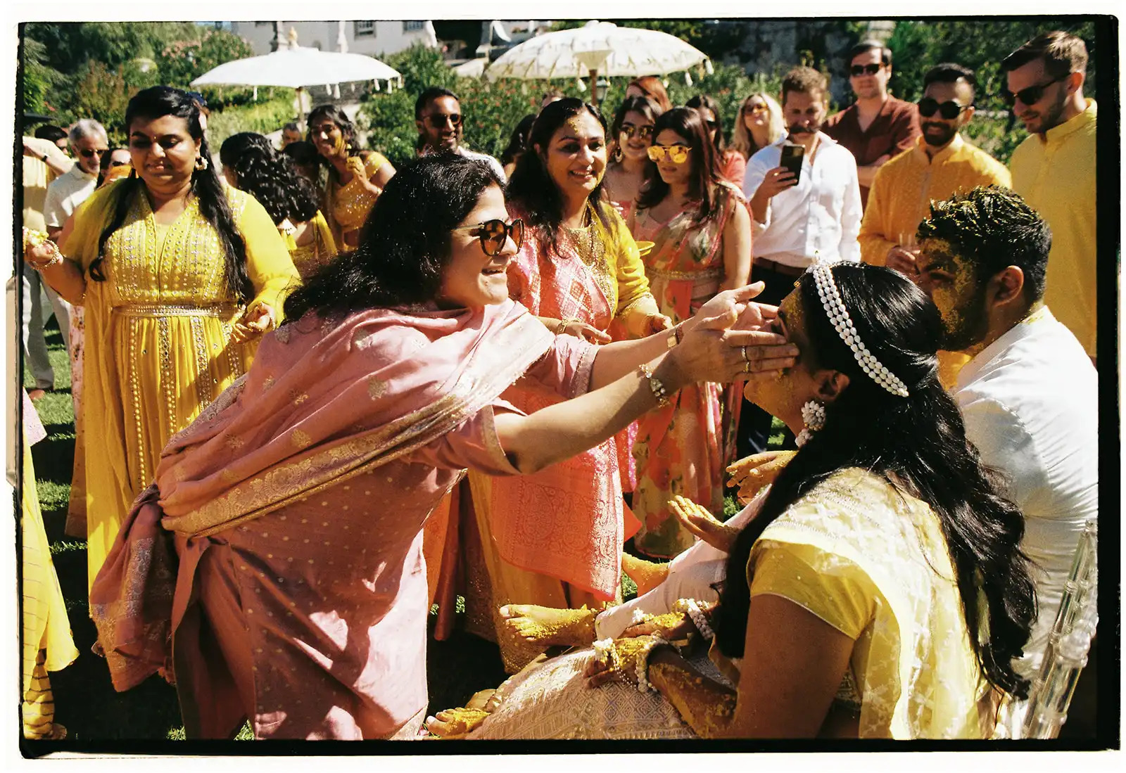 Indian wedding in Portugal. Haldi ceremony moment with decor in yellow and gold. Bride and groom surronded by guests in yellow outfits enjoying the blessings.
