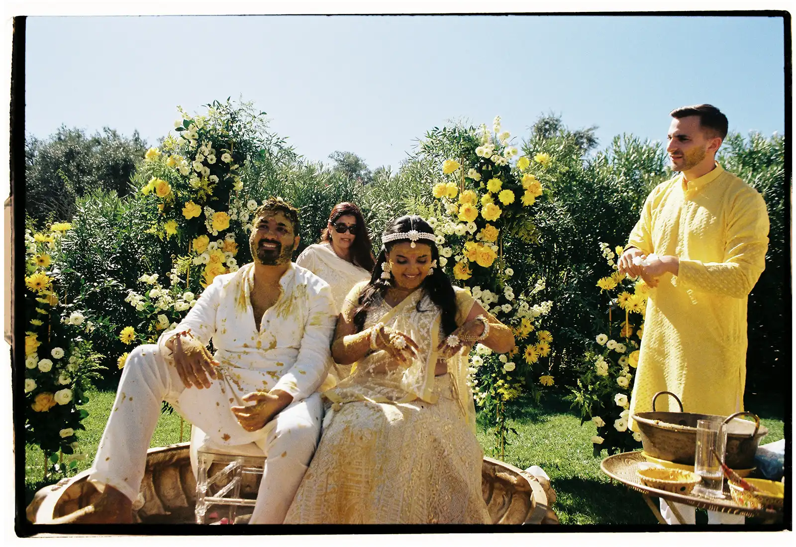 Indian wedding in Portugal. Haldi ceremony moment with decor in yellow and gold. Bride and groom inside the badjot surronded by guests in yellow outfits.