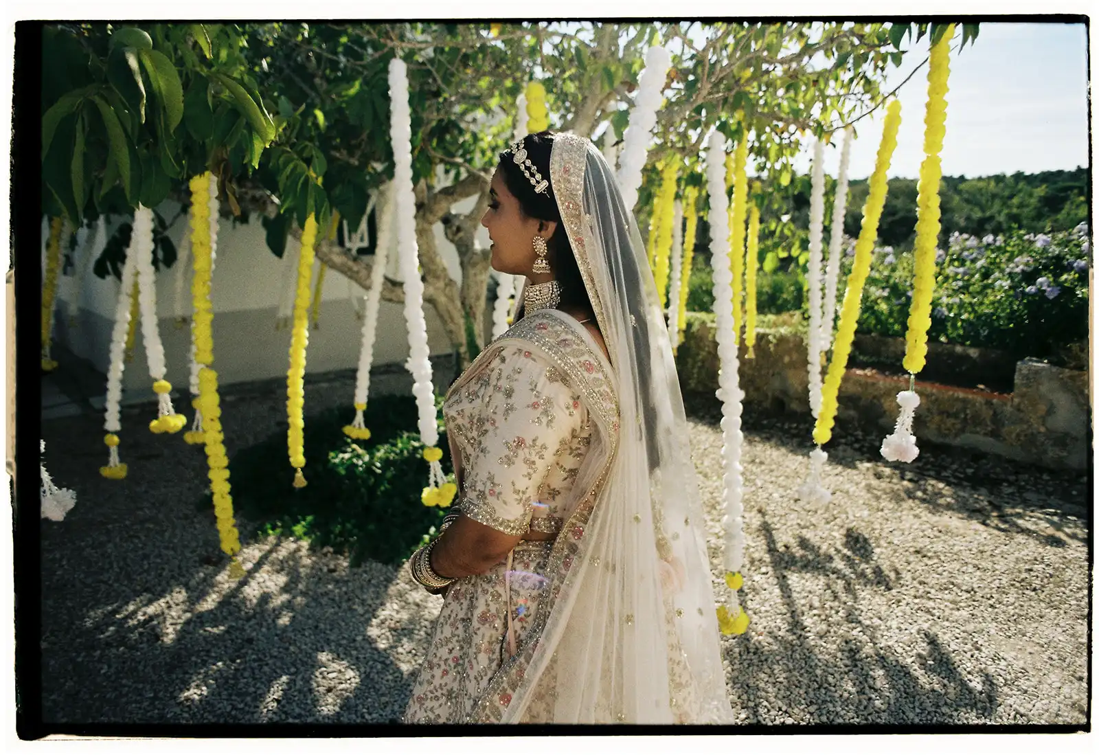 Indian bride in a Indian beige and gold tradicional outfit. Background whit a tree with white and yellow hanging garlands. Indian wedding in Portugal.