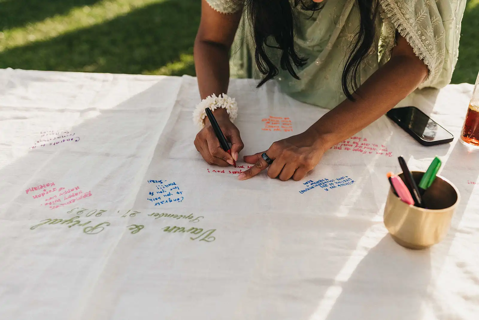 A creative and fun guest book, tablecloth embroidered with the names of the bride and groom. Guest writing her whishes with fabric pen.