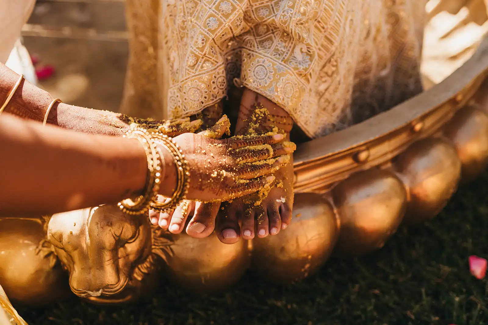 A close-up of the Haldi ceremony, with a guest applying turmeric paste to the bride's feet for purification. Indian Haldi ceremony in portugal with yellow and gold decoration details.