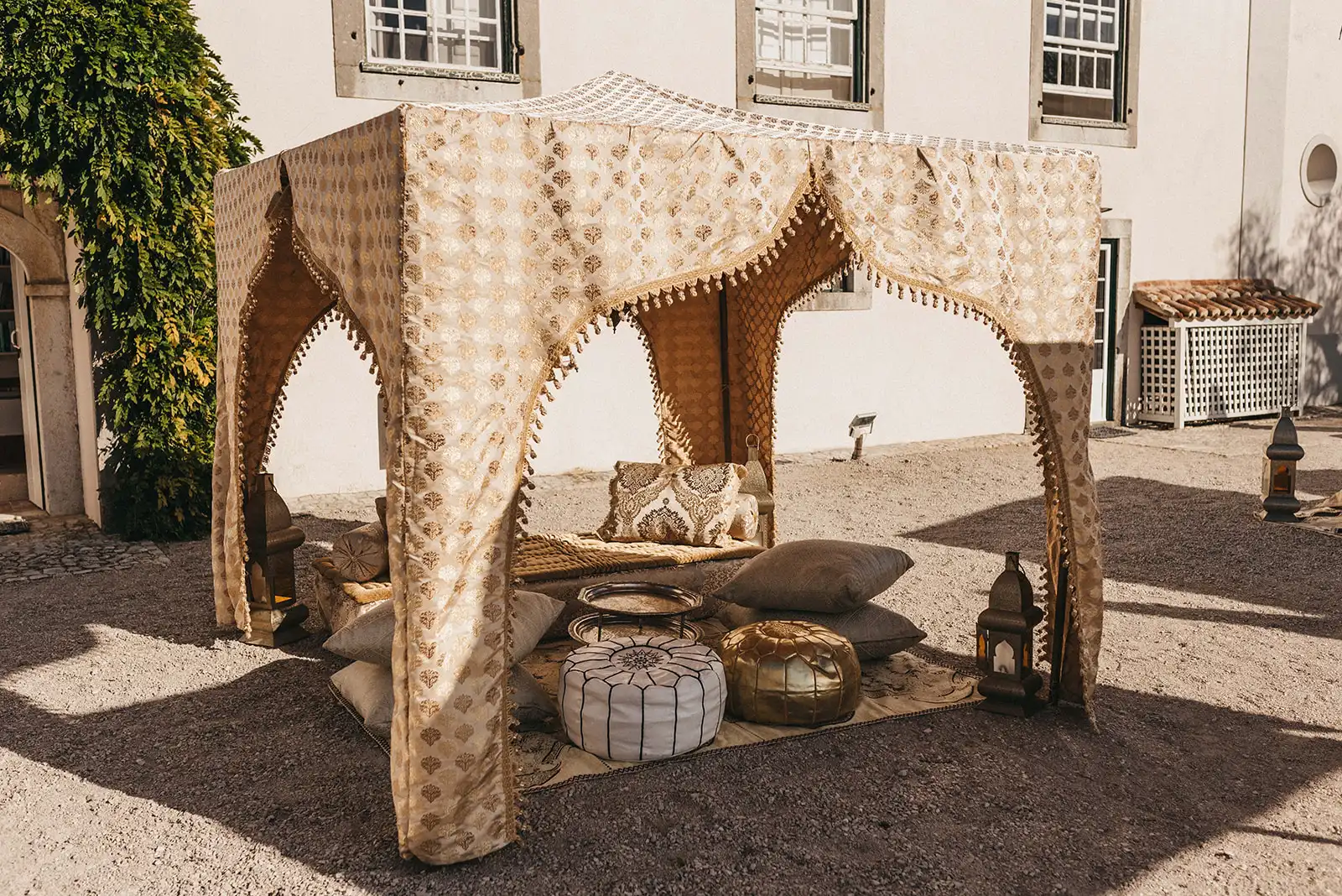 Indian wedding in Portugal with a gold and white lounge for cocktail moment. Gold dossel with cushions, lanterns, puffs and rugs.